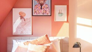 A bedroom with a sloped ceiling, a bed with pink bedding, and artwork on the walls.