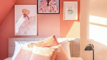 A bedroom with a sloped ceiling, a bed with pink bedding, and artwork on the walls.