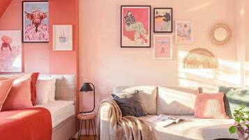 A cozy living room with a sofa, a small table, and a lamp. There are framed artworks on the wall.