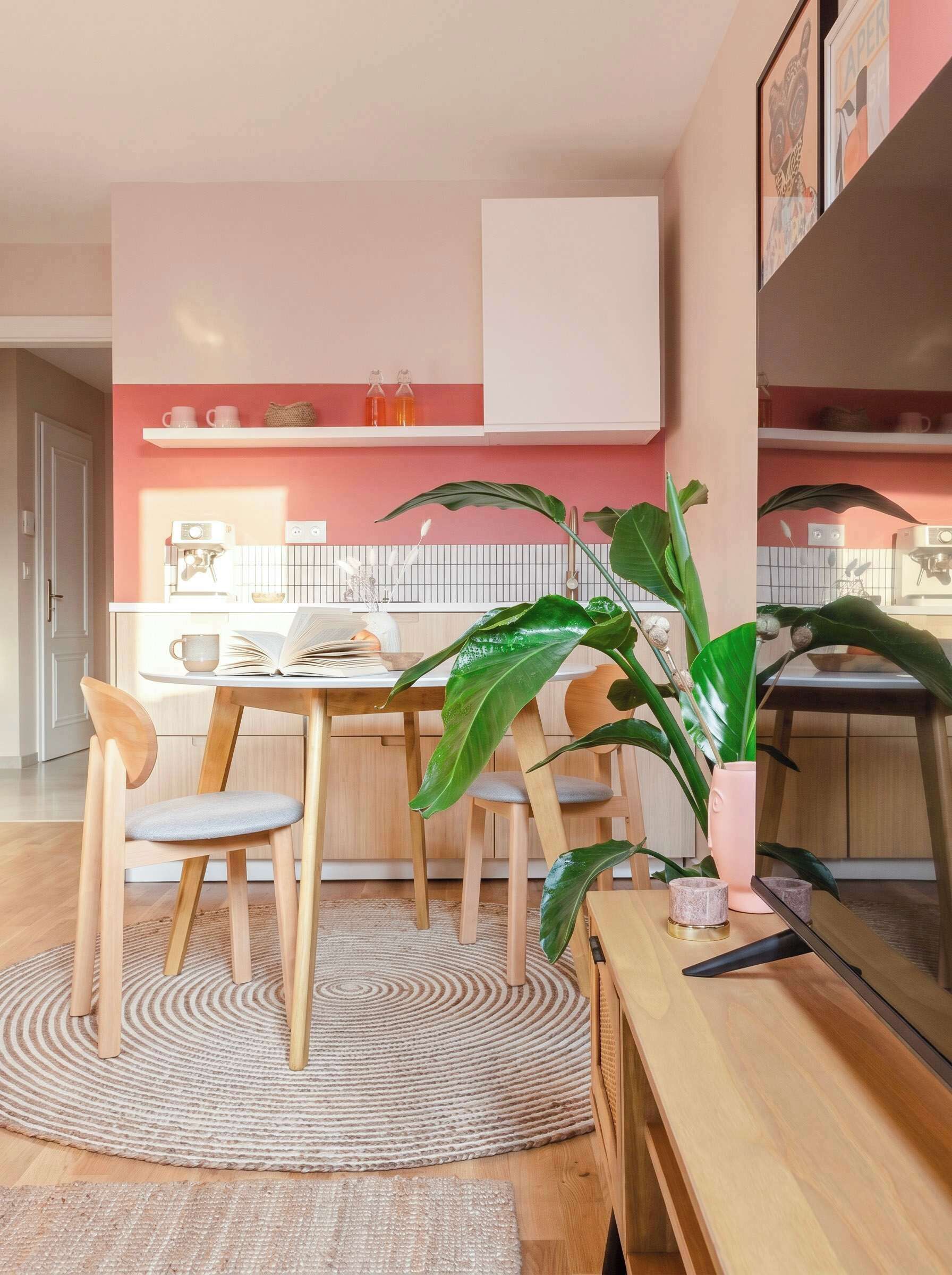 A modern kitchen with a dining area, featuring a coffee machine, a plant, and a wooden dining table with chairs.