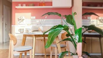 Una cucina moderna con zona pranzo, che include una macchina per il caffè, una pianta e un tavolo da pranzo in legno con sedie.