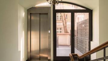 An interior view of a building with a closed elevator, a glass door leading outside, and a wooden staircase railing.