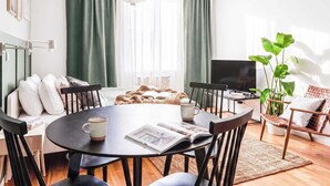 Ein modernes Wohnzimmer mit einem runden Esstisch, schwarzen Stühlen, einem Couchtisch, einem Fernseher und einer großen Pflanze.