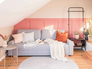 Uma sala de estar acolhedora com um sofá cinza, uma mesa redonda pequena e uma parede de destaque rosa.