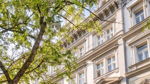 Ein mehrgeschossiges Gebäude mit klassischer Architektur, das einen zentralen Eingang mit einem dekorativen Bogen und zahlreiche Fenster aufweist.