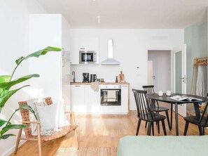 Cozinha compacta com eletrodomésticos modernos, sala de jantar com mesa e cadeiras, e uma grande planta verde.