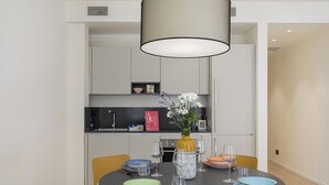 Ein moderner Essbereich mit einem runden Tisch, gedeckt für vier Personen, umgeben von gelben Stühlen. Auf dem Tisch steht eine Vase mit Blumen, sowie verschiedene Geschirrteile und Gläser.