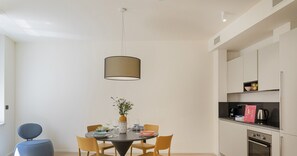 A modern kitchen with white cabinets, a built-in oven, and a dining area with a round table and chairs.