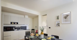 Una cocina moderna con armarios blancos, un microondas y una estufa. Hay una mesa de comedor con platos y tazones de colores.