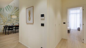 A hotel room with a dining area, a wall with a pineapple artwork, a thermostat, and a door leading to another room.