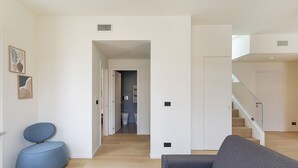 Una sala de estar moderna con un sofá gris, un sillón azul y una escalera que sube a otro nivel.