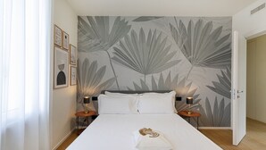 Un dormitorio con una cama grande, dos mesitas de noche con lámparas, una pared con estampado de hojas y una puerta a otra habitación.