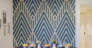 Ein Essbereich mit Wand in geometrischem Muster, Tisch für vier Personen gedeckt mit Tellern, Gläsern und Blumen in einer Vase.