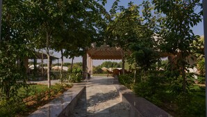 A stone pathway leading to a covered pavilion with a tiled roof, surrounded by greenery and trees. - Aangan Resort (Jhunjhunu)