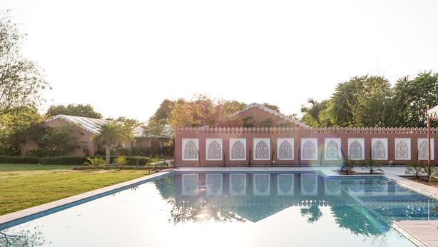 A swimming pool with a decorative fence, surrounded by greenery and trees. - Aangan Resort (Jhunjhunu)