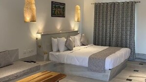 A bedroom with a bed, bedside tables, a bench, and a painting on the wall. - Aangan Resort (Jhunjhunu)