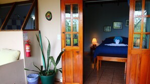 A room with a bed, a window, a door, a potted plant, and a fire extinguisher.
