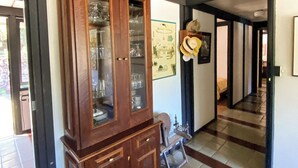 A hallway with a wooden cabinet containing glassware, a hat on the wall, and a tiled floor. - Spectacular Farm in Ibiúna (Ibiuna)