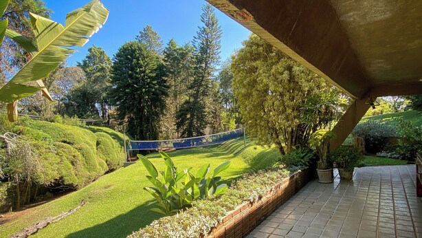 A covered patio with a view of a well-maintained garden, a tennis court, and a brick pathway. - Spectacular Farm in Ibiúna (Ibiuna)