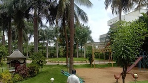 Ein Mann trägt ein langes Objekt und geht auf einem gepflasterten Weg in einem Park mit Palmen und einem Spielplatz.