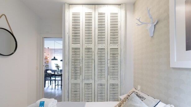A bedroom with a bed, a white wall, a wooden door with shutters, and a mounted deer head. - Astoria - baskeyrentals (San Sebastián)