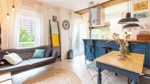 A cozy living room with a sofa, a coffee table, and a view of a cityscape through large windows. - Astoria - baskeyrentals (San Sebastián)