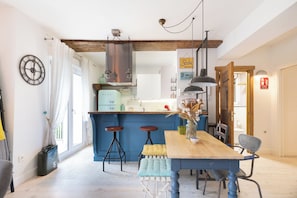 A modern kitchen with a blue accent wall, a wooden dining table with stools, and a visible clock on the wall. - Astoria - baskeyrentals (San Sebastián)