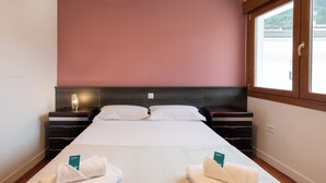 A double bed with a dark headboard, two bedside tables, a window with a view, and a pink wall.