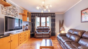 A living room with a TV, leather sofas, wooden cabinets, and a large window with curtains.