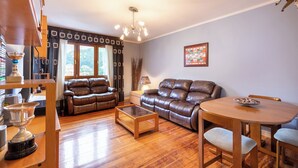A cozy living room with a brown leather sofa, a wooden coffee table, and a dining area with a round table and chairs.