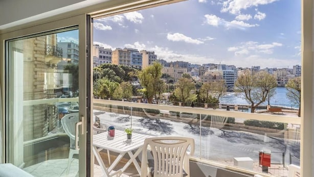 A balcony with a table and chairs, overlooking a cityscape and a body of water.