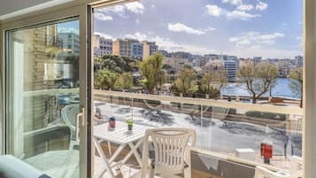 A balcony with a table and chairs, overlooking a cityscape and a body of water.