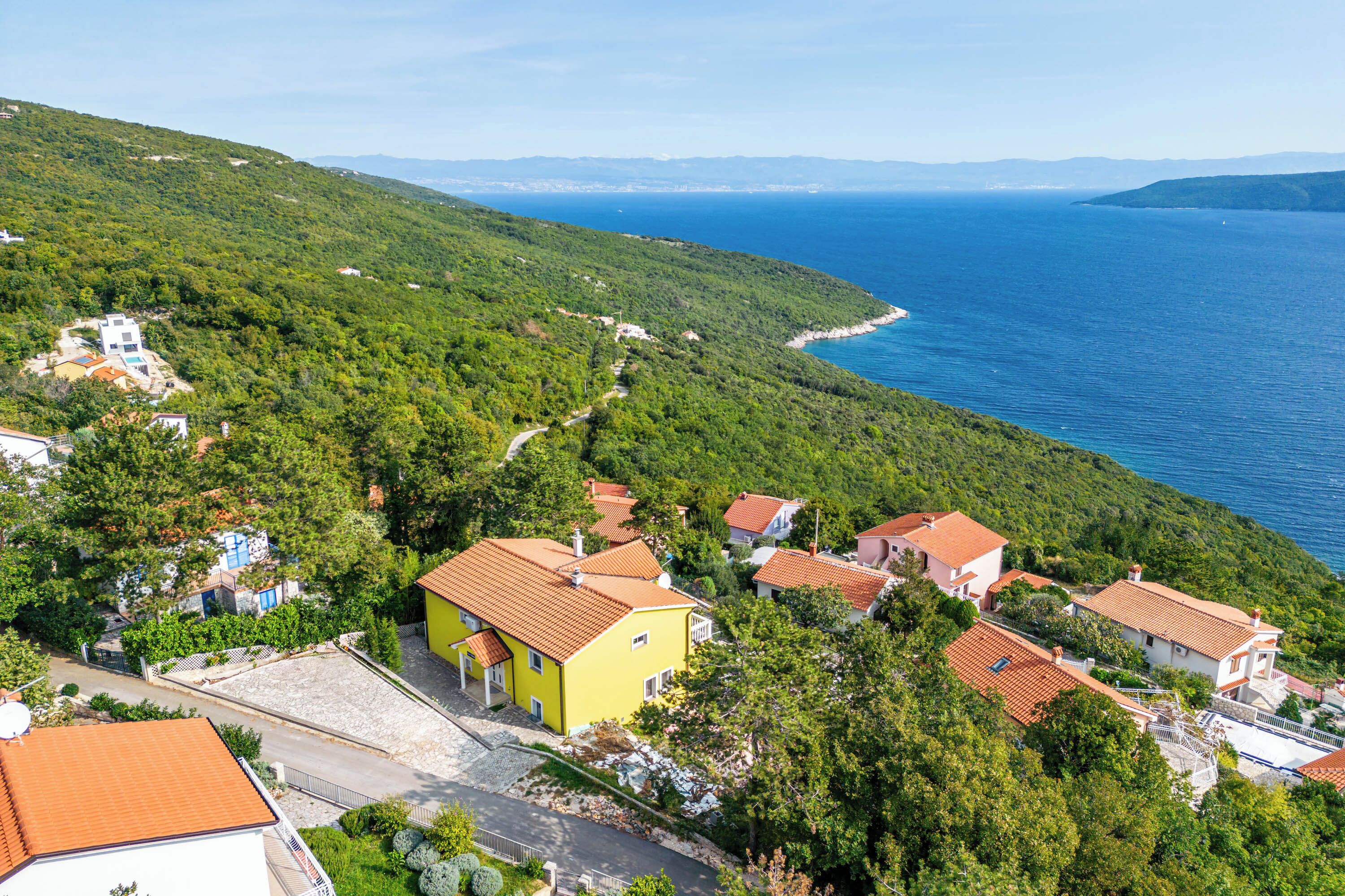 A coastal village with terraced houses, a clear view of the sea, and a winding road.
