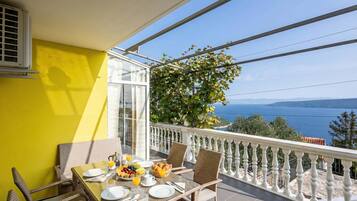 A balcony with a table set for breakfast, a view of the sea, and a yellow wall.