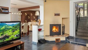 Een moderne woonkamer met een televisie, open haard, eethoek en trap.
