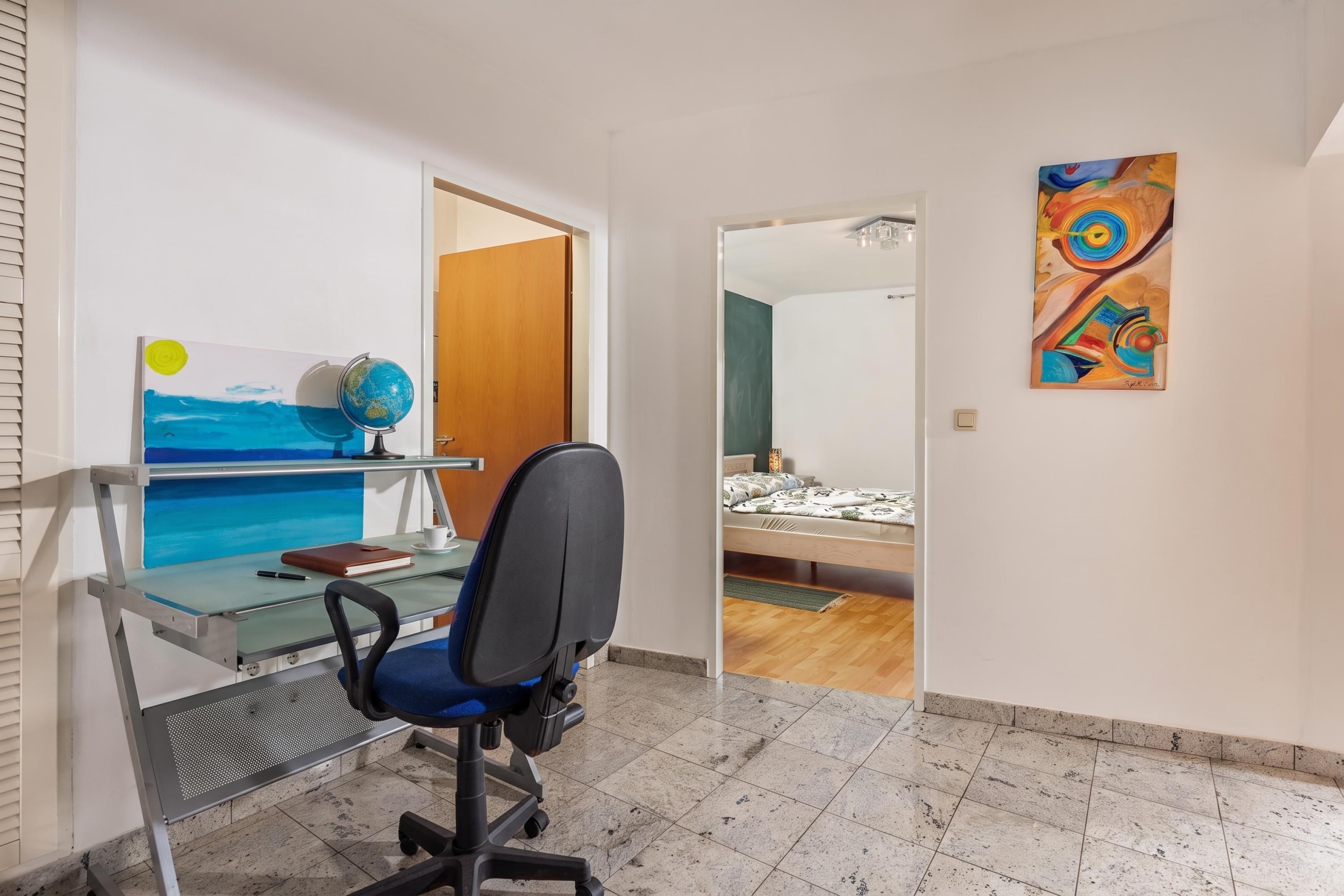 A bedroom with a bed, a desk with a chair, a globe, and a painting on the wall.