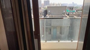 A balcony with a city view, a bed, and a window with curtains. - Earth View Residency  (Noida)