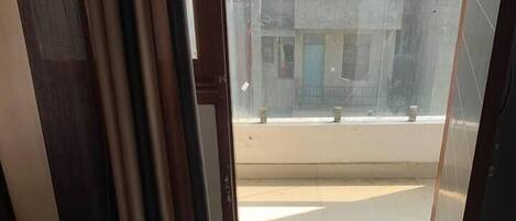 Uma varanda com vista para a cidade, uma cama e uma janela com cortinas.