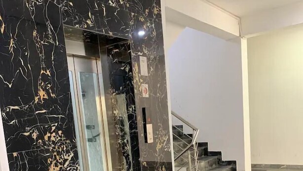 A modern elevator with a black marble finish, a staircase with metal railings, and a plain white wall. - Earth View Residency  (Noida)