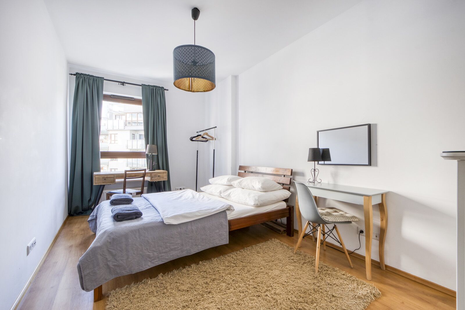 A modern bedroom with a bed, desk, and a hanging light fixture.