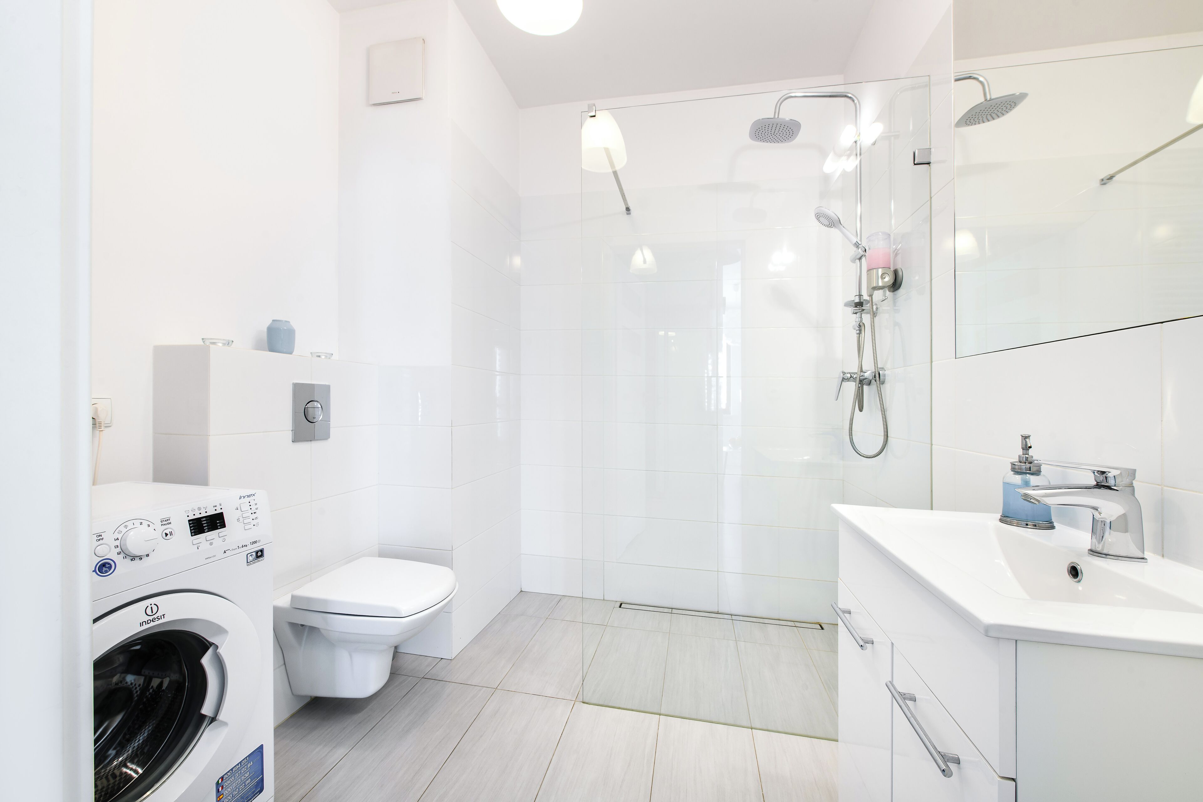 A modern bathroom with a washing machine, toilet, shower, and sink.