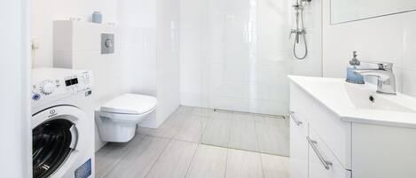 A modern bathroom with a washing machine, toilet, shower, and sink.