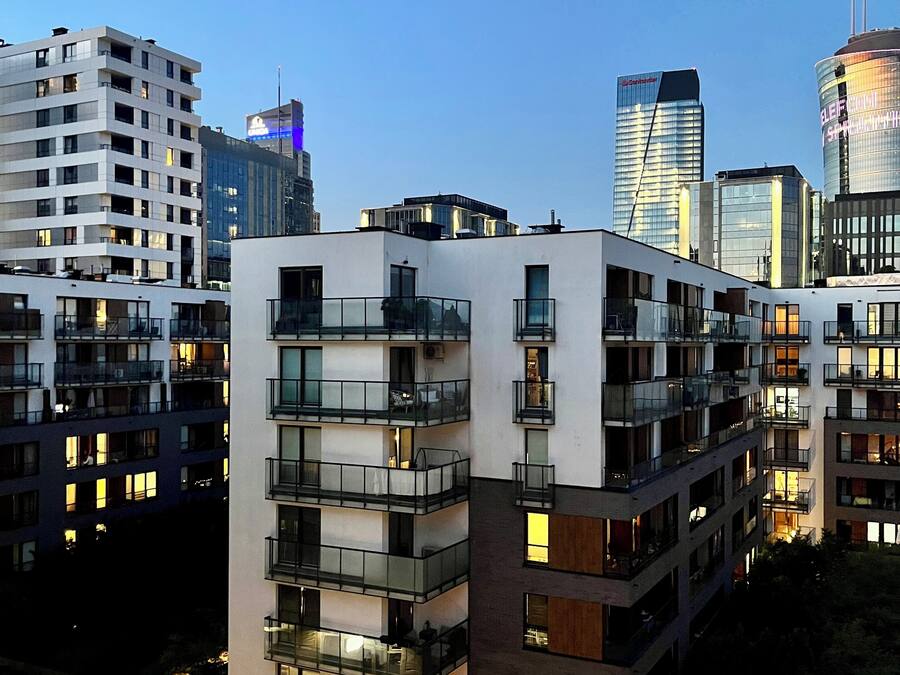 Um edifício residencial de vários andares com varandas, área de estacionamento e vista para o horizonte da cidade.