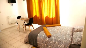 Quarto com cama, escrivaninha com cadeira, televisão fixada na parede e janela com cortinas.