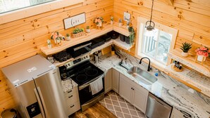 Une cuisine compacte aux murs en bois, dotée d’appareils électroménagers en acier inoxydable et d’une fenêtre donnant sur l’extérieur.