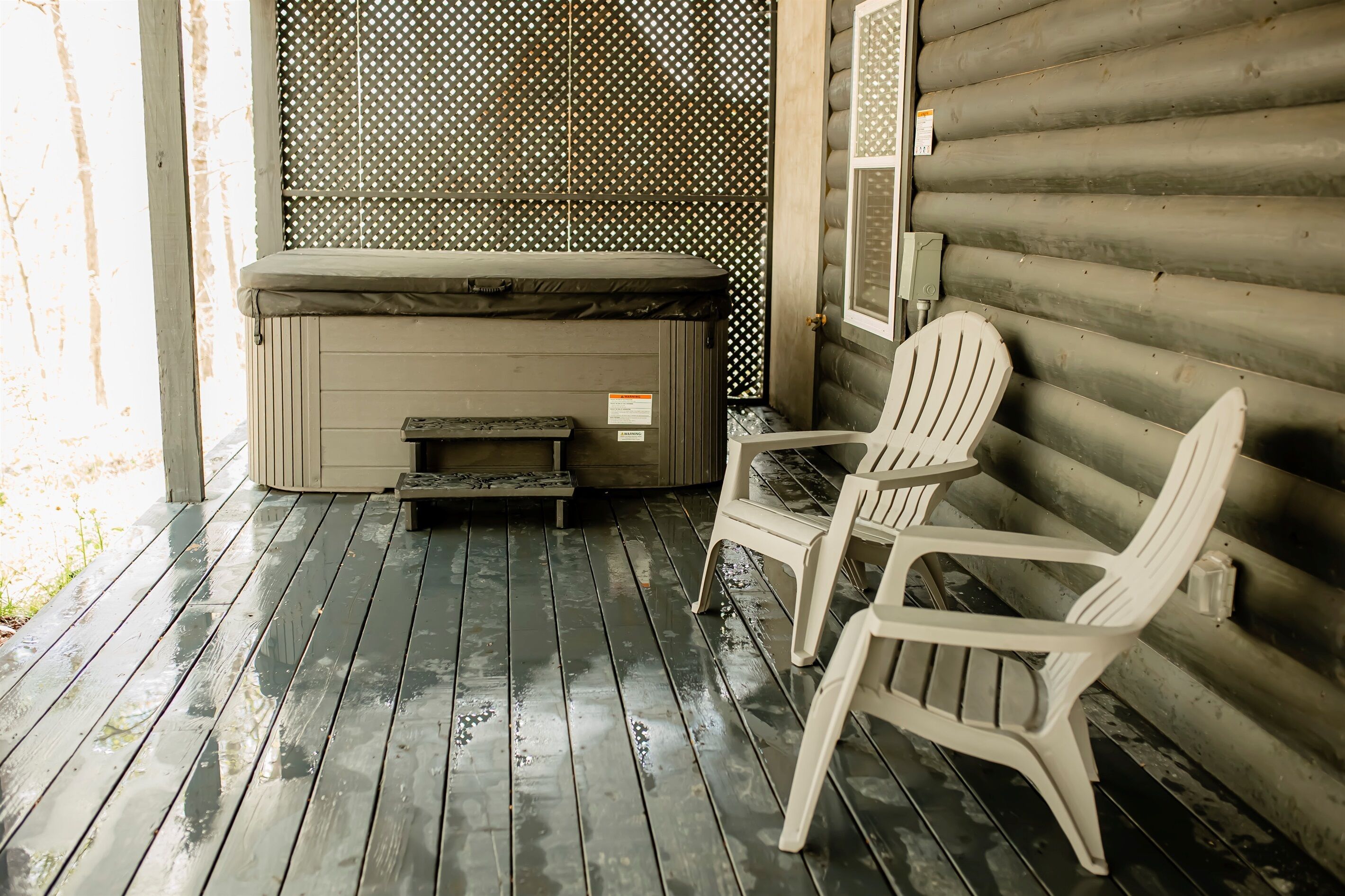 A wooden deck with a hot tub, two Adirondack chairs, and a wooden wall.