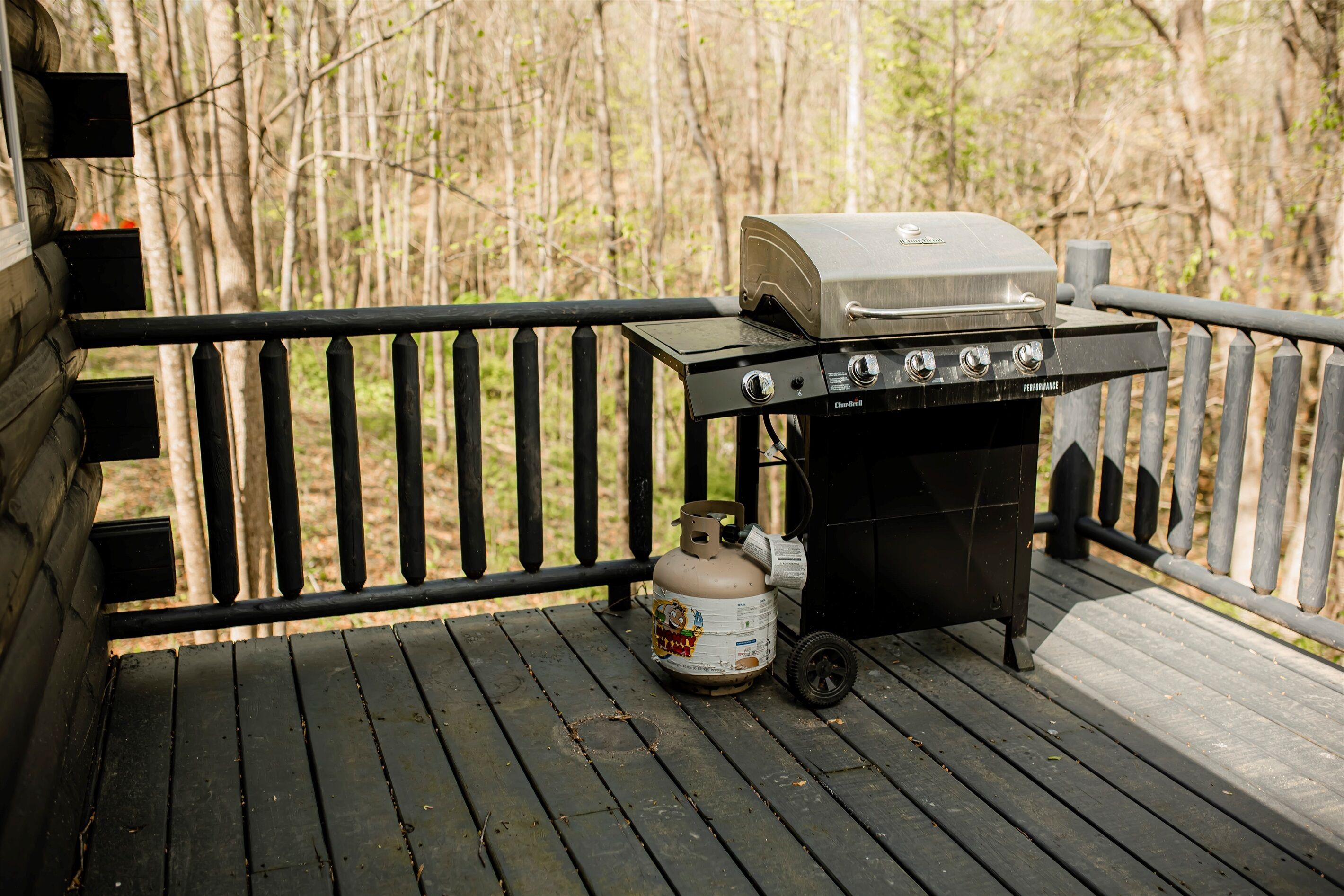 A portable grill with a propane tank on a wooden deck.