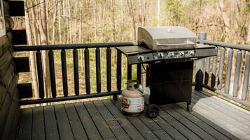A portable grill with a propane tank on a wooden deck.