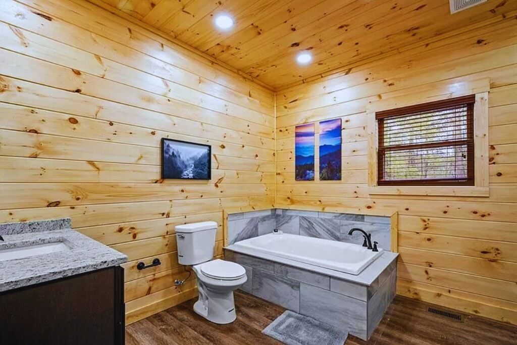 A wooden cabin bathroom with a bathtub, toilet, and sink.