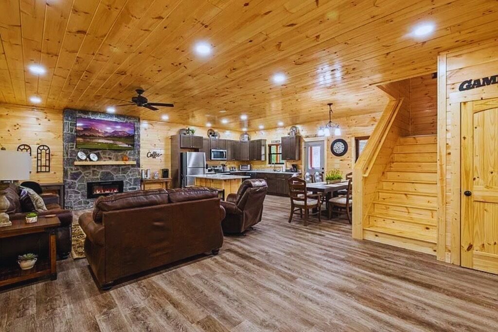 A cozy cabin interior with a living room, fireplace, kitchen, and a staircase leading to a loft bedroom.